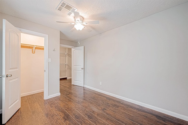 unfurnished bedroom with a walk in closet, a textured ceiling, ceiling fan, dark wood-type flooring, and a closet