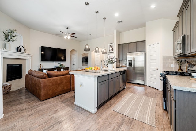 kitchen with hanging light fixtures, light hardwood / wood-style flooring, an island with sink, appliances with stainless steel finishes, and tasteful backsplash