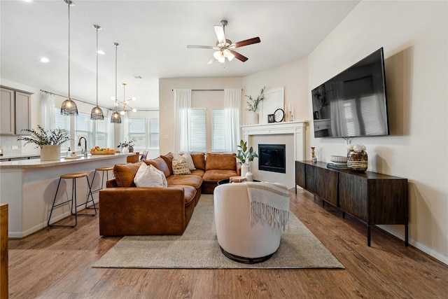 living room featuring ceiling fan, light hardwood / wood-style floors, sink, and a tiled fireplace