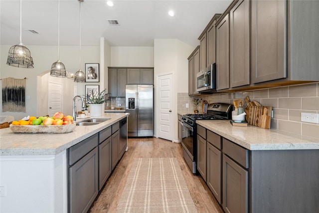 kitchen with appliances with stainless steel finishes, backsplash, sink, light hardwood / wood-style flooring, and hanging light fixtures