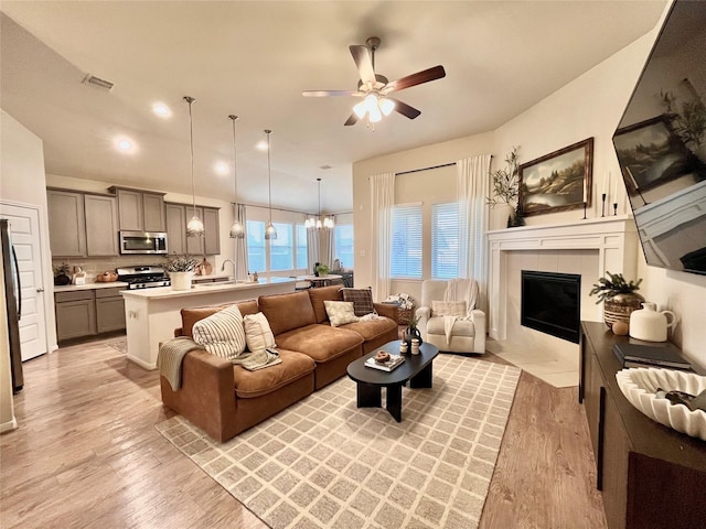 living room featuring a fireplace, ceiling fan with notable chandelier, light hardwood / wood-style floors, and sink