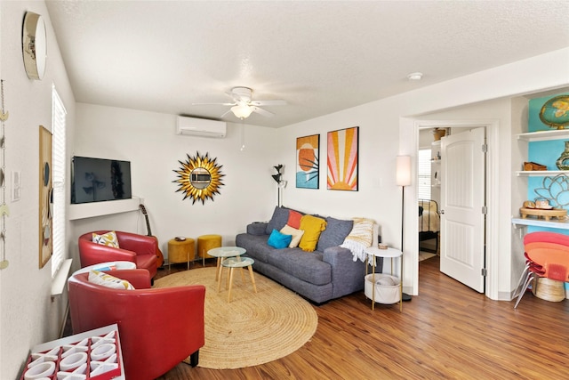 living room featuring wood-type flooring, a textured ceiling, a wall unit AC, and ceiling fan