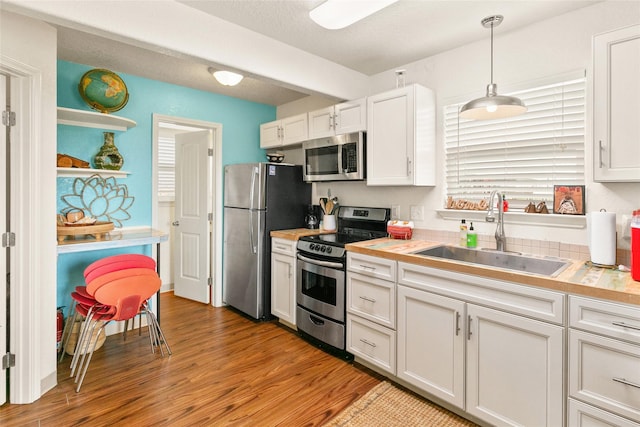 kitchen with stainless steel appliances, sink, light hardwood / wood-style flooring, white cabinetry, and hanging light fixtures