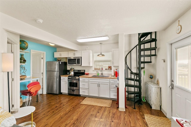 kitchen with hanging light fixtures, a textured ceiling, appliances with stainless steel finishes, light hardwood / wood-style floors, and white cabinetry