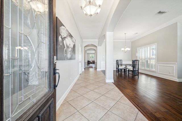 tiled foyer featuring ornamental molding, a healthy amount of sunlight, and a notable chandelier