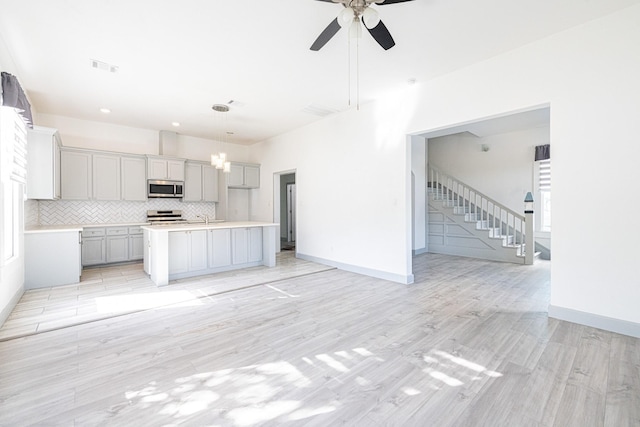 kitchen with appliances with stainless steel finishes, light wood-type flooring, a kitchen island with sink, decorative light fixtures, and gray cabinets