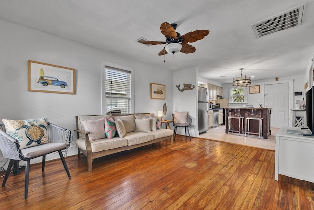 living room featuring ceiling fan with notable chandelier, light hardwood / wood-style floors, and a wealth of natural light