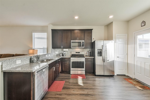 kitchen featuring light stone counters, stainless steel appliances, a sink, dark brown cabinets, and backsplash