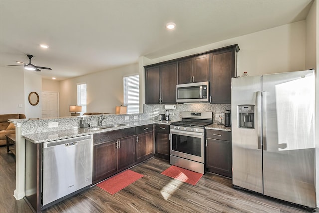 kitchen with dark wood finished floors, stainless steel appliances, a sink, light stone countertops, and a peninsula