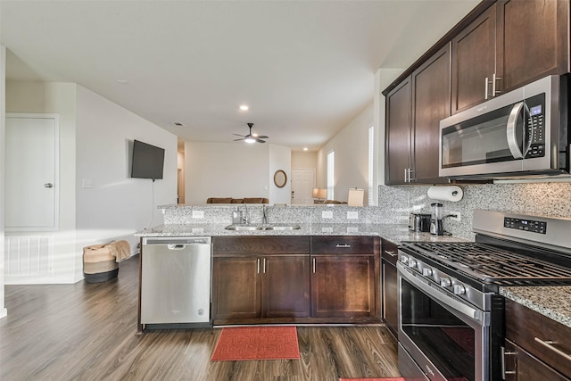 kitchen featuring a peninsula, appliances with stainless steel finishes, a sink, and light stone counters