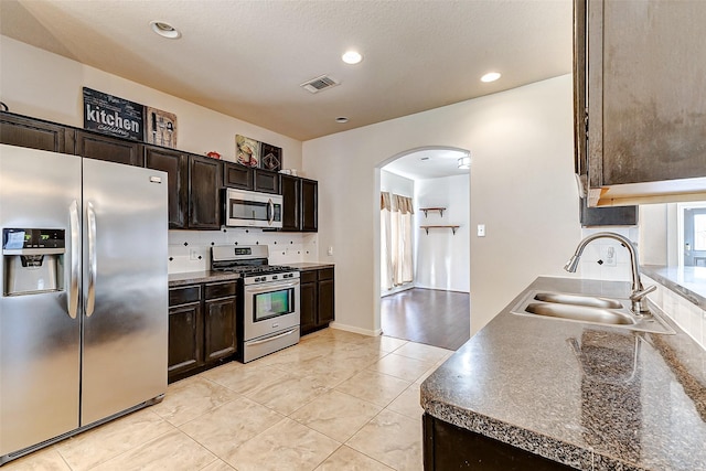 kitchen featuring arched walkways, a sink, visible vents, appliances with stainless steel finishes, and dark countertops