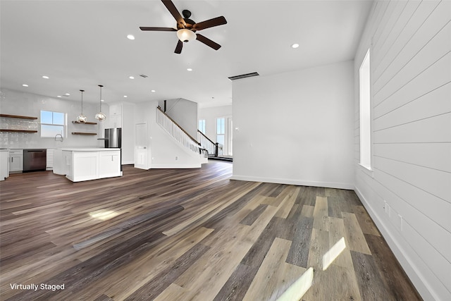 unfurnished living room featuring plenty of natural light, ceiling fan, and dark hardwood / wood-style flooring