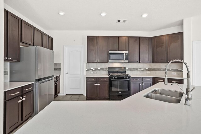 kitchen with sink, backsplash, dark brown cabinets, light tile patterned flooring, and appliances with stainless steel finishes