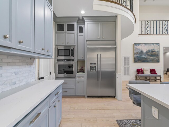 kitchen with light stone countertops, tasteful backsplash, built in appliances, light hardwood / wood-style flooring, and gray cabinets