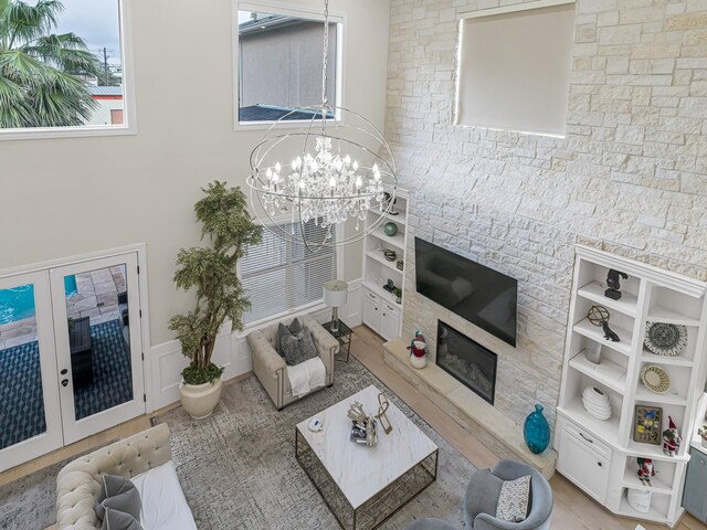 living room featuring a stone fireplace, a chandelier, french doors, and wood-type flooring