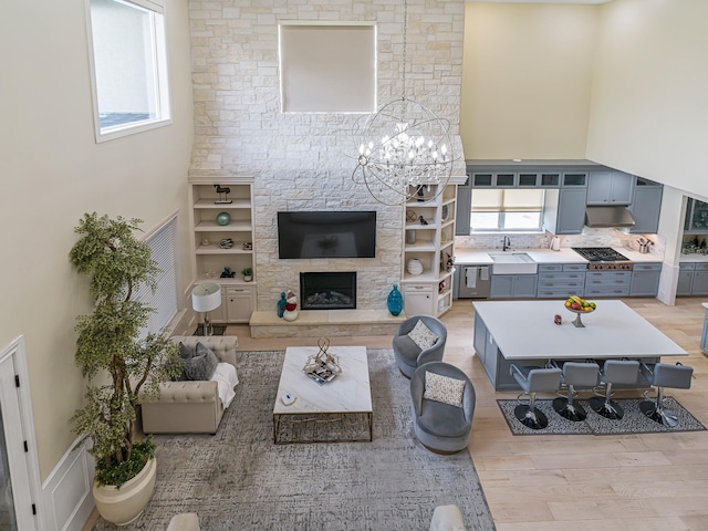 living area featuring light wood-type flooring, a fireplace, a towering ceiling, and an inviting chandelier