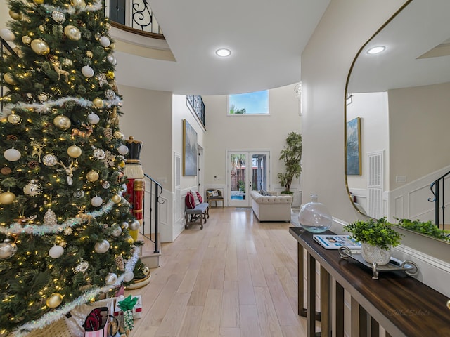 hallway with french doors, a towering ceiling, and light hardwood / wood-style flooring