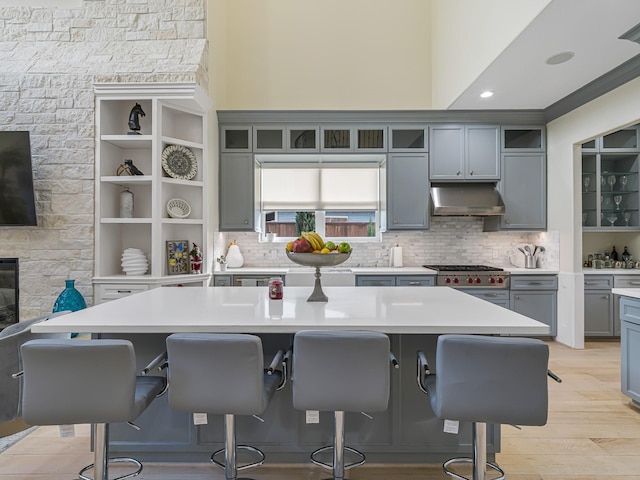 kitchen featuring stainless steel range, a center island, light hardwood / wood-style flooring, range hood, and a breakfast bar