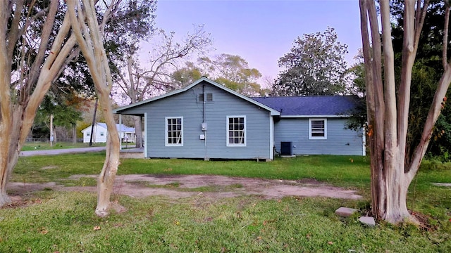 back house at dusk featuring a lawn and central AC