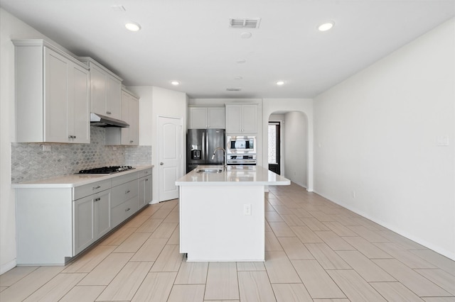 kitchen with backsplash, a kitchen island with sink, sink, and stainless steel appliances