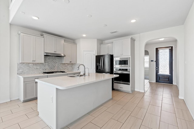 kitchen featuring tasteful backsplash, stainless steel appliances, a kitchen island with sink, sink, and white cabinetry