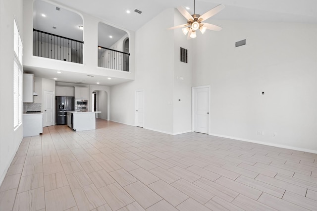 unfurnished living room with ceiling fan and a high ceiling