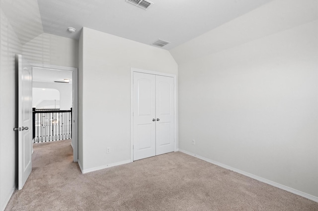 unfurnished bedroom featuring light carpet, a closet, and lofted ceiling