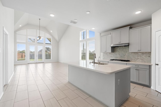 kitchen featuring tasteful backsplash, stainless steel gas cooktop, a kitchen island with sink, sink, and gray cabinets