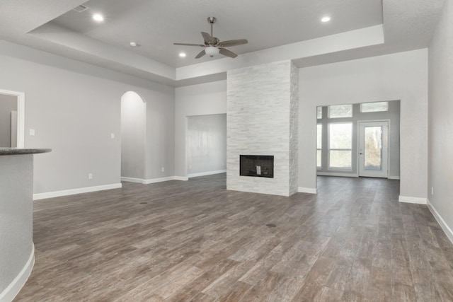 unfurnished living room featuring dark hardwood / wood-style flooring, a raised ceiling, ceiling fan, and a stone fireplace