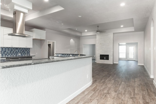 kitchen with a raised ceiling, island range hood, white cabinetry, and dark hardwood / wood-style floors