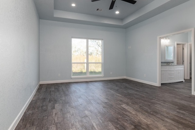 unfurnished room featuring a raised ceiling, ceiling fan, and dark hardwood / wood-style flooring