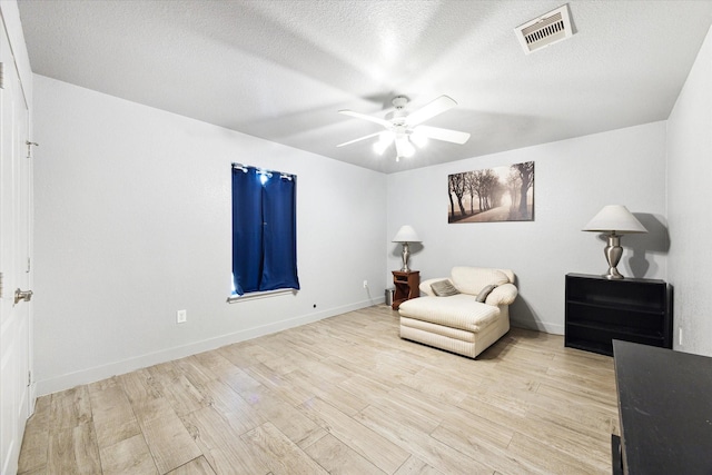 living area featuring ceiling fan, light hardwood / wood-style floors, and a textured ceiling