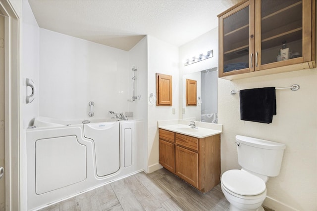 bathroom featuring vanity, a bath, toilet, a textured ceiling, and wood-type flooring