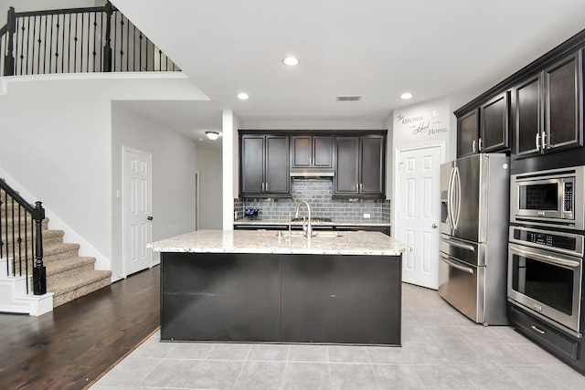 kitchen featuring light stone countertops, stainless steel appliances, light hardwood / wood-style flooring, and a center island with sink