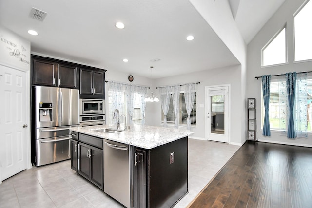 kitchen with appliances with stainless steel finishes, sink, pendant lighting, light hardwood / wood-style flooring, and an island with sink