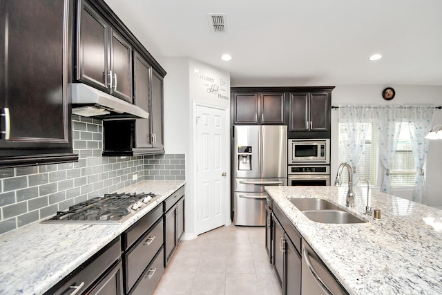 kitchen with appliances with stainless steel finishes, backsplash, light stone counters, sink, and light tile patterned floors