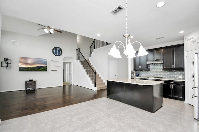 kitchen with pendant lighting, a center island with sink, ceiling fan with notable chandelier, light wood-type flooring, and stainless steel gas cooktop