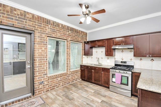 kitchen with sink, stainless steel gas stove, light stone countertops, ornamental molding, and light hardwood / wood-style floors