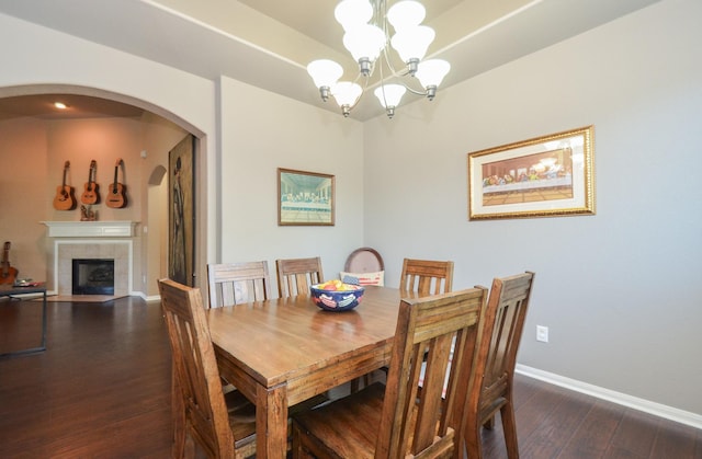 dining area featuring a tiled fireplace, dark wood-type flooring, and an inviting chandelier