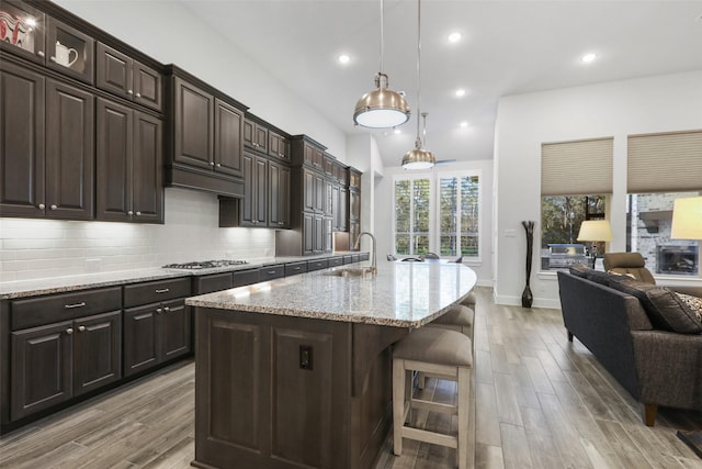 kitchen with sink, hanging light fixtures, an island with sink, a kitchen bar, and dark brown cabinetry