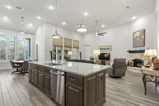 kitchen with a brick fireplace, dark brown cabinetry, sink, dishwasher, and an island with sink