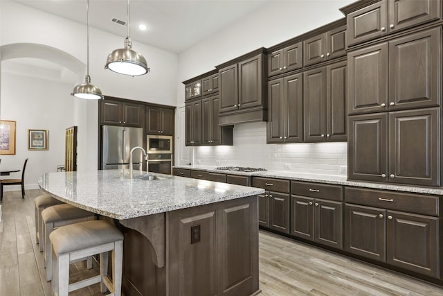 kitchen featuring a kitchen bar, appliances with stainless steel finishes, a kitchen island with sink, sink, and decorative light fixtures