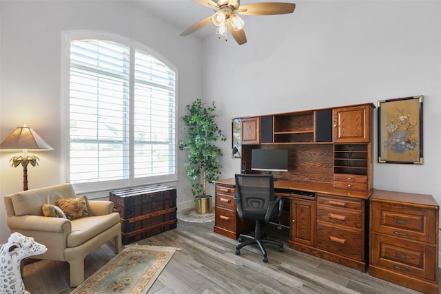 home office with light wood-type flooring, ceiling fan, and a healthy amount of sunlight