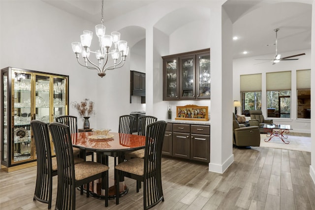 dining room with ceiling fan with notable chandelier, light hardwood / wood-style floors, and high vaulted ceiling