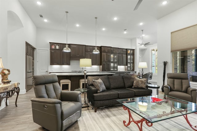 living room featuring ceiling fan, light wood-type flooring, and a towering ceiling