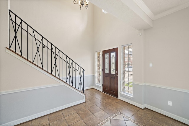 foyer entrance with crown molding, tile patterned flooring, a healthy amount of sunlight, and a notable chandelier