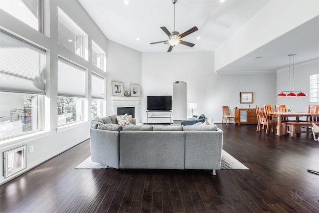 living room featuring a towering ceiling, crown molding, dark hardwood / wood-style flooring, and ceiling fan