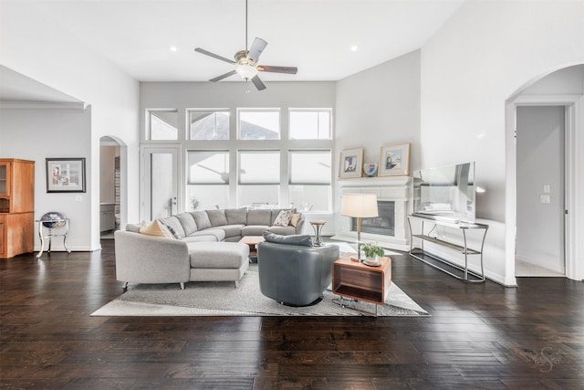 living room with a high ceiling, crown molding, ceiling fan, and dark wood-type flooring