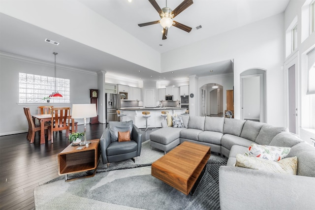 living room with ceiling fan, dark hardwood / wood-style flooring, a towering ceiling, and crown molding