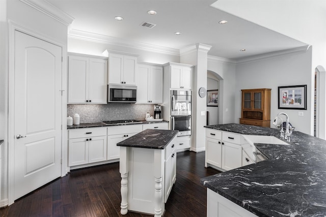 kitchen with white cabinets, appliances with stainless steel finishes, dark hardwood / wood-style flooring, and a center island with sink